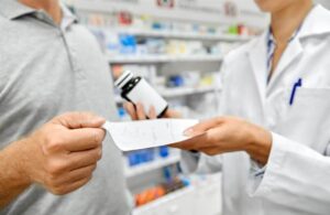 Pharmacist with drug taking prescription from male customer at drugstore.